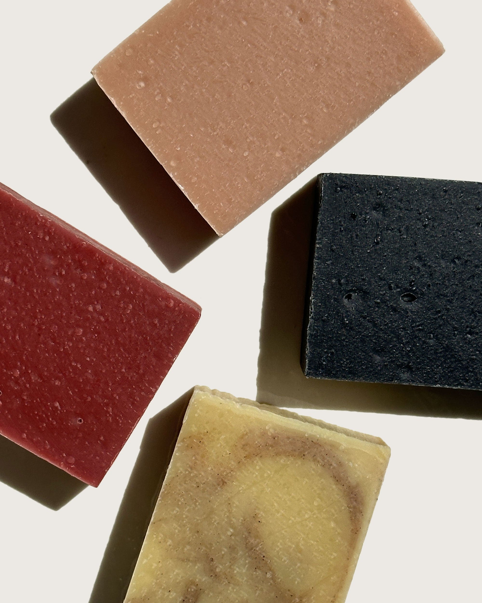 Three different colored bar soaps: one is red, the second is black, and the third is a light brown color.