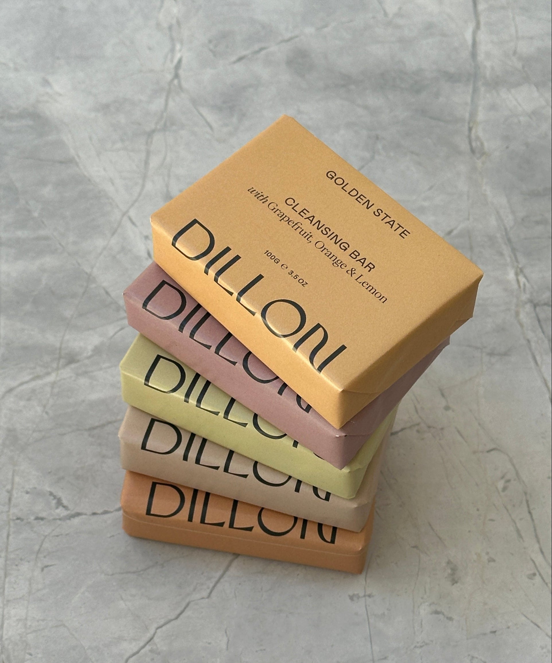 Four Dillon soap bars of different colors stacked on a textured gray surface