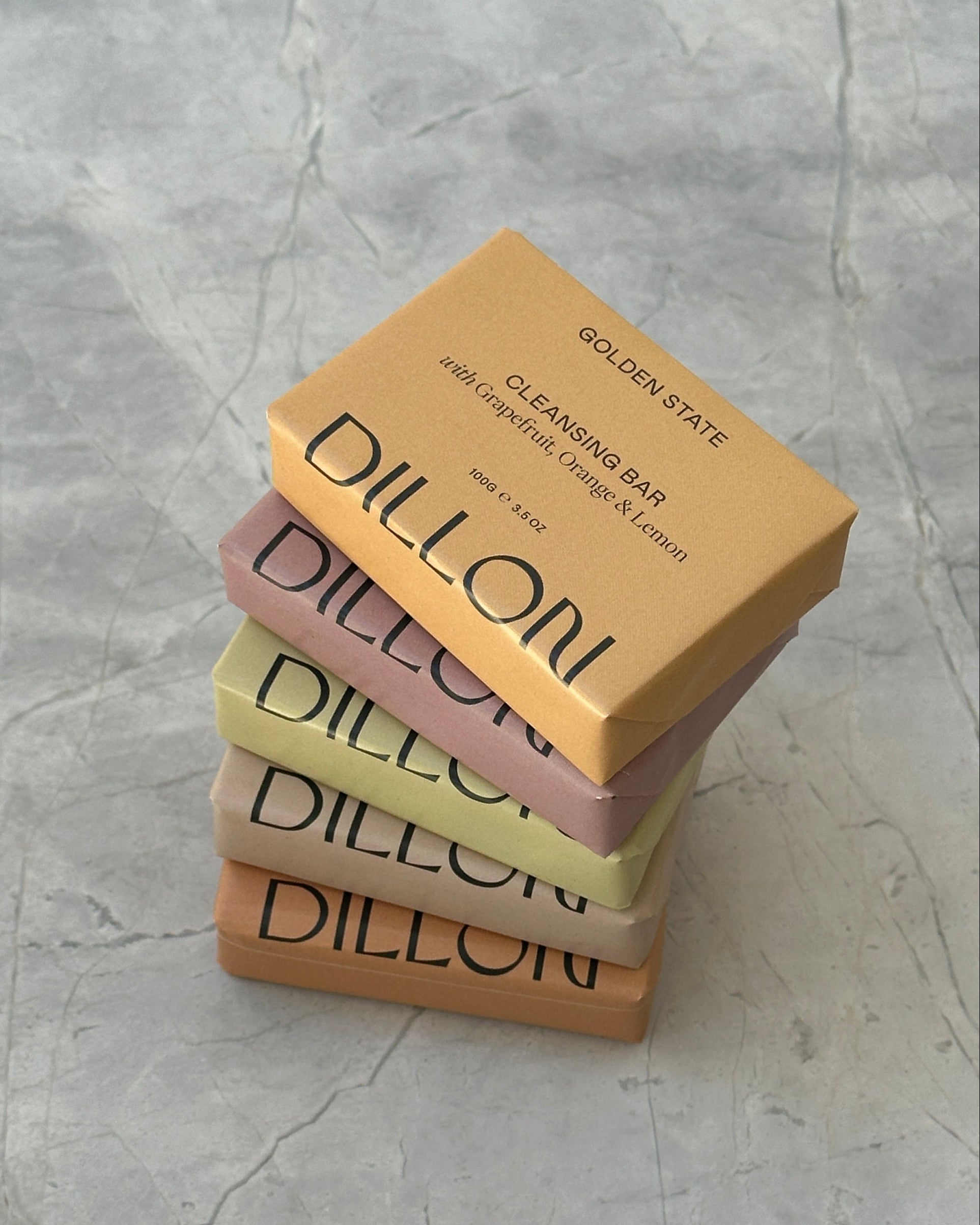 Four Dillon soap bars of different colors stacked on a textured gray surface