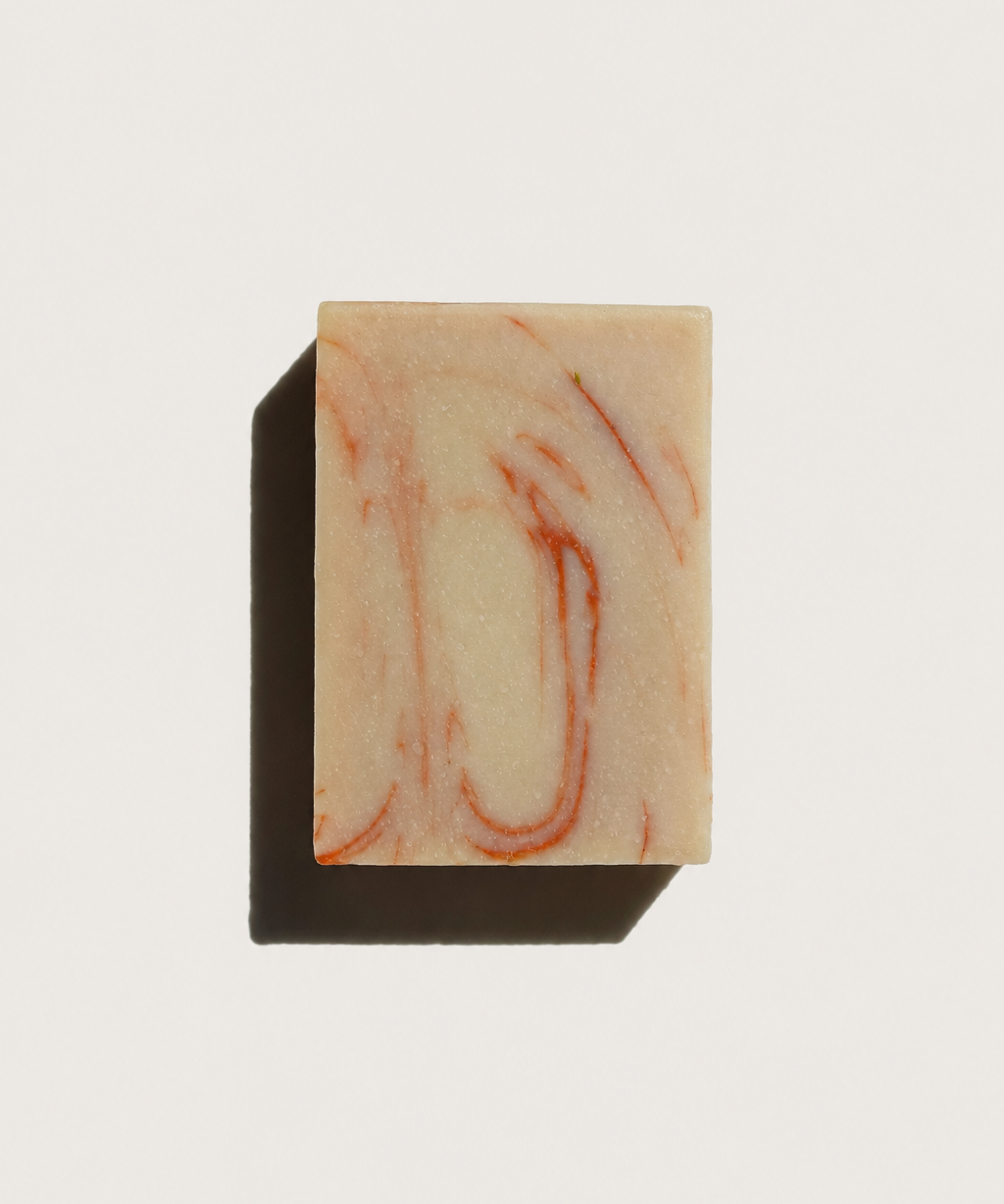 A rectangular bar of soap with a cream-colored base and reddish-orange marbled swirls, casting a dark shadow on a plain white background.