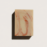 A rectangular bar of soap with a cream-colored base and reddish-orange marbled swirls, casting a dark shadow on a plain white background.