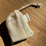 A small cream-colored mesh drawstring pouch with a white tag reading 'DILLON' placed on a wooden surface.