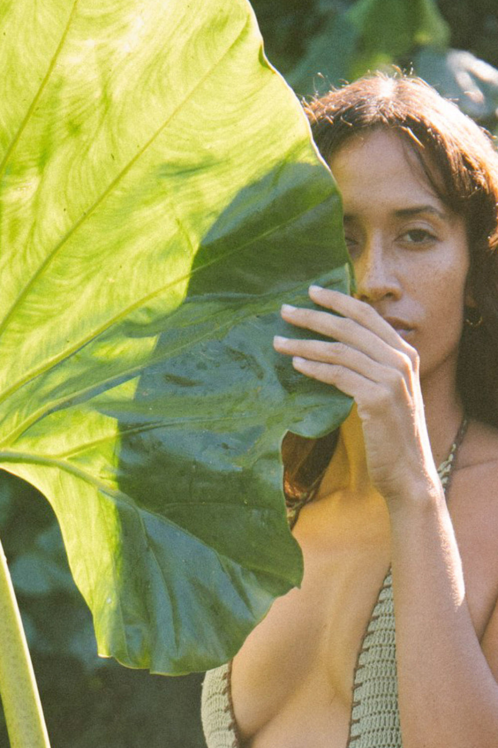 Woman holding a large green leaf in front of her face with a natural background