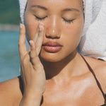 Woman applying face oil on a beach