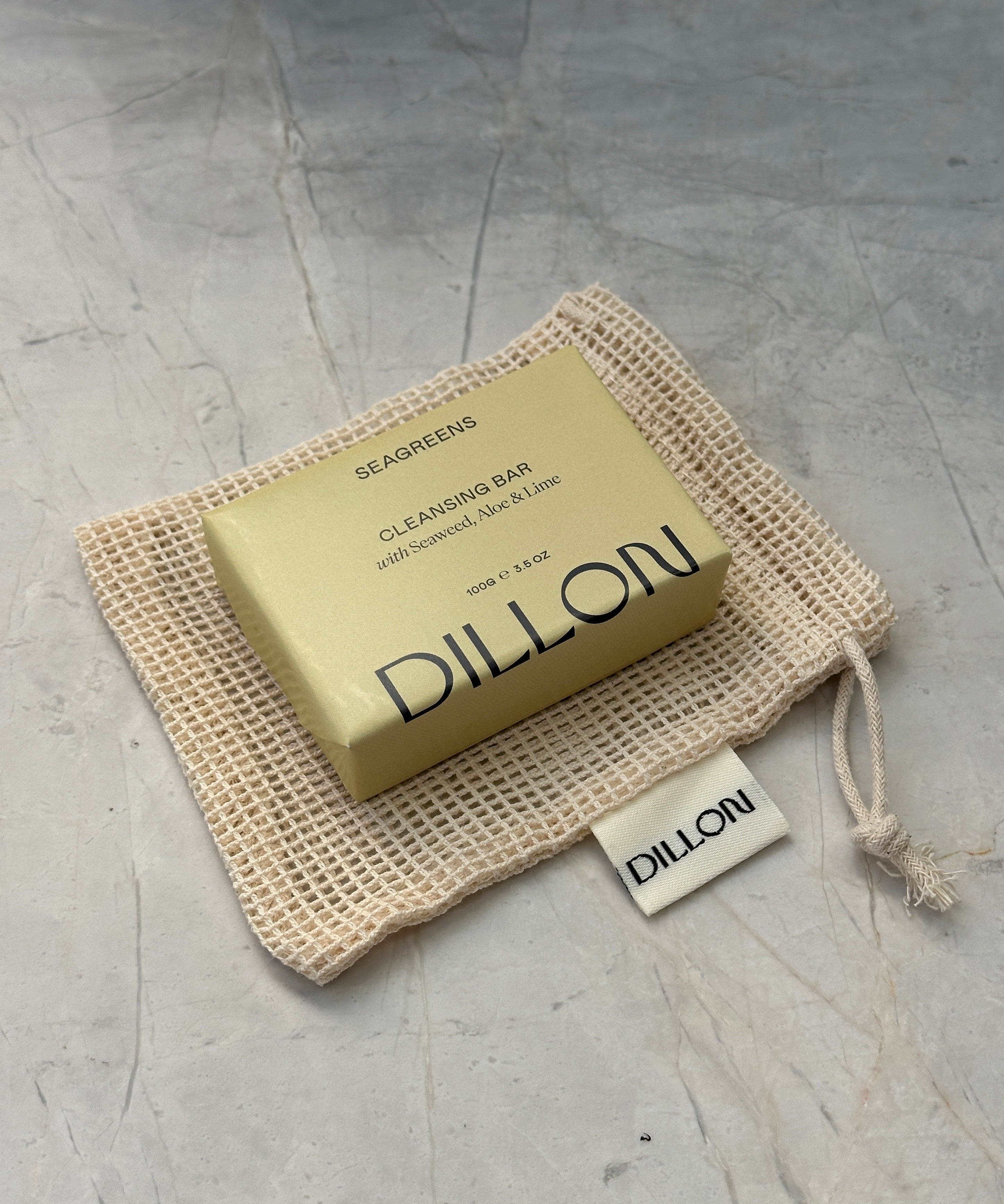 A bar of Dillon soap in a beige mesh drawstring pouch on a textured gray surface.