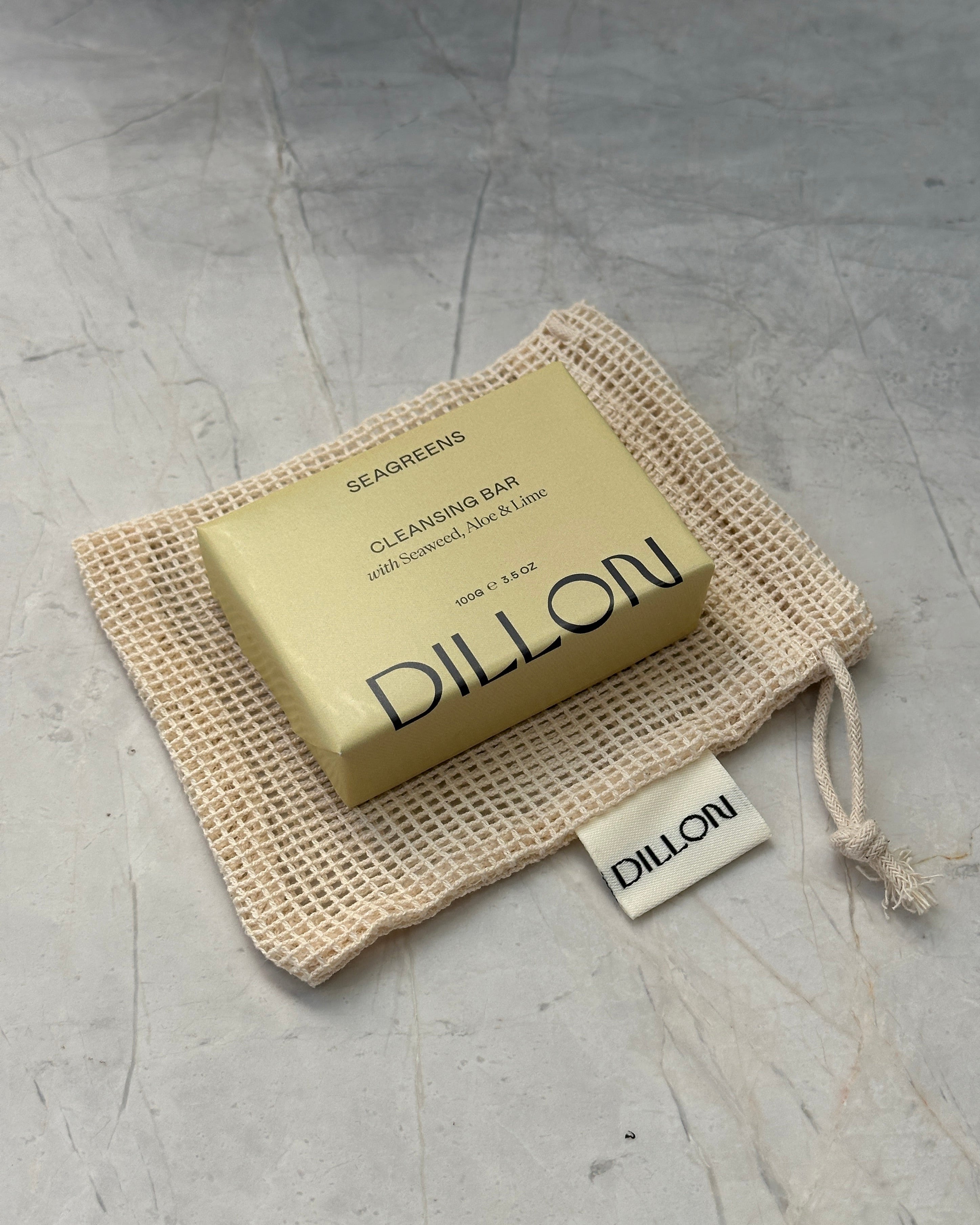 A bar of Dillon soap in a beige mesh drawstring pouch on a textured gray surface.
