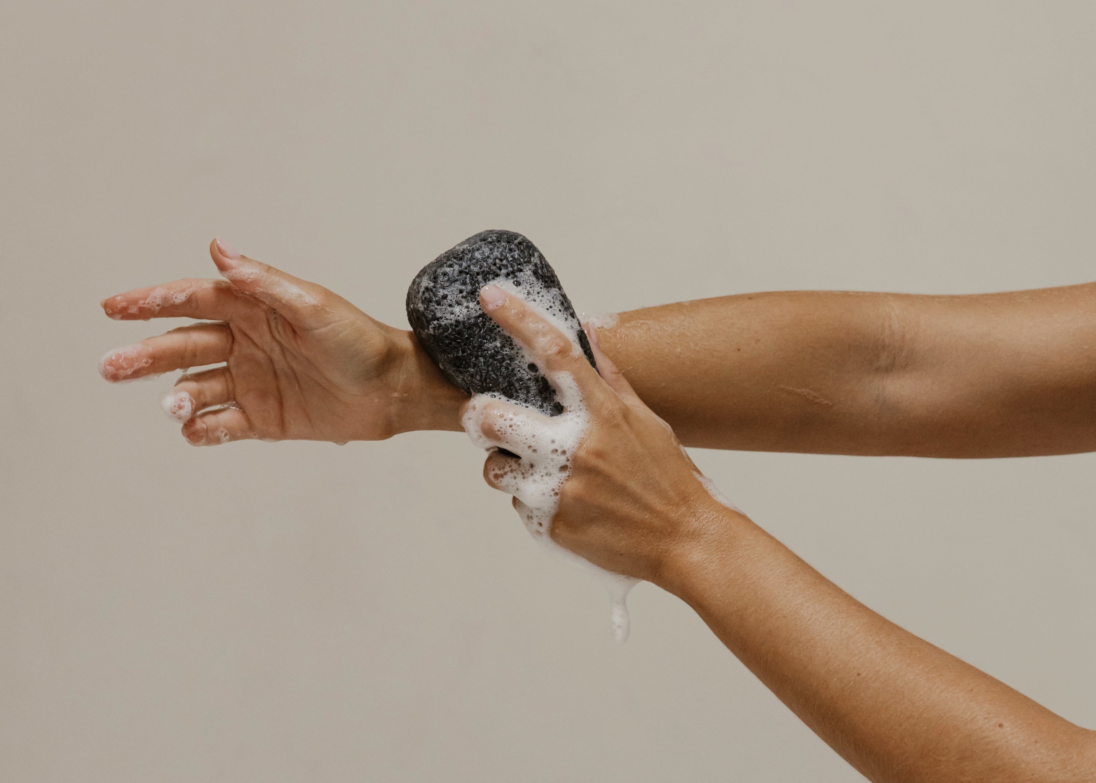 Person scrubbing their arm with a black konjac sponge against a plain background